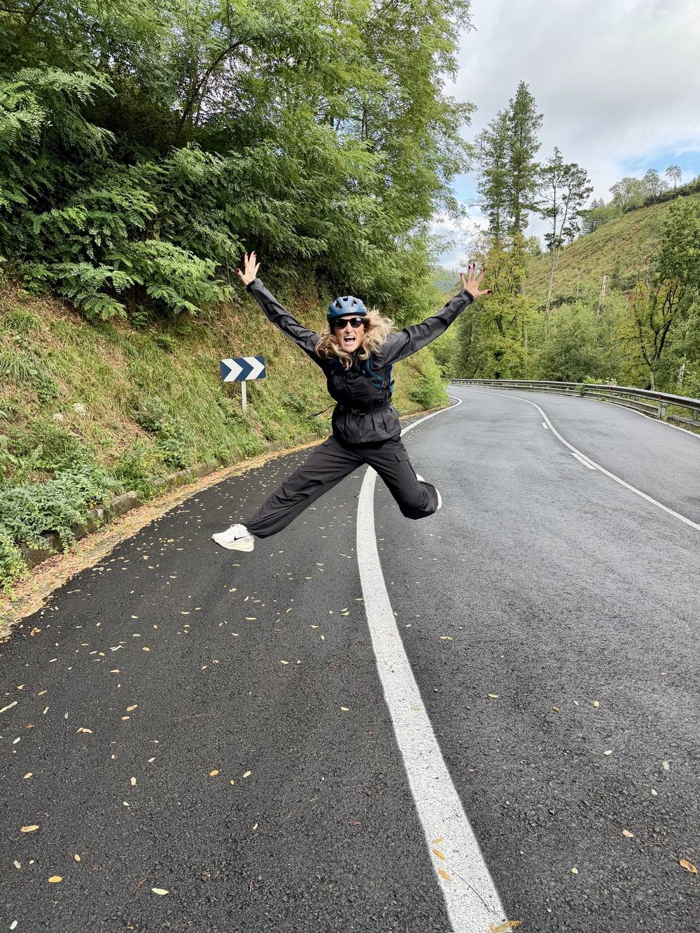 Jenn jumping joyfully on a mountain road during her Camino cycling journey in Spain.